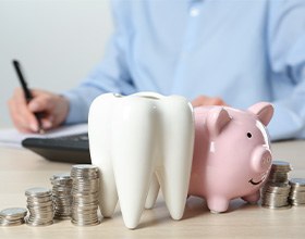 A ceramic model of a tooth next to a piggy bank and stacked coins