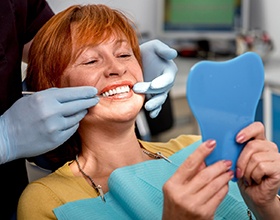 woman smiling while looking into dental mirror 