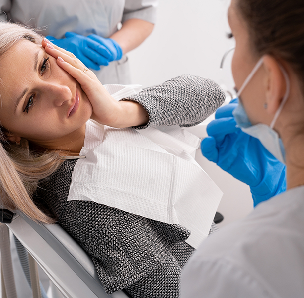 Woman holding her cheek in pain while talking to her emergency dentist in Boca Raton