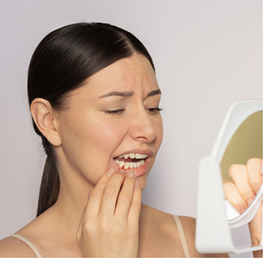 Woman looking at her red gums in a mirror