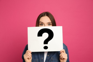 Woman holding up a card with a question mark on it to cover her mouth